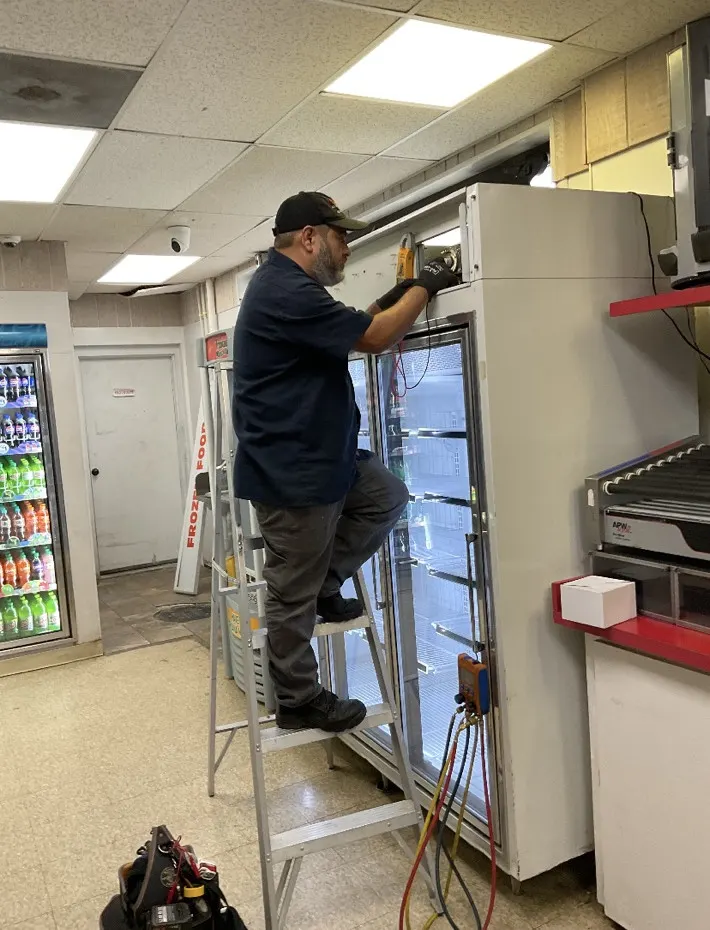 Technician repairing a glass-door display cooler at a convenience store in Rockford, IL